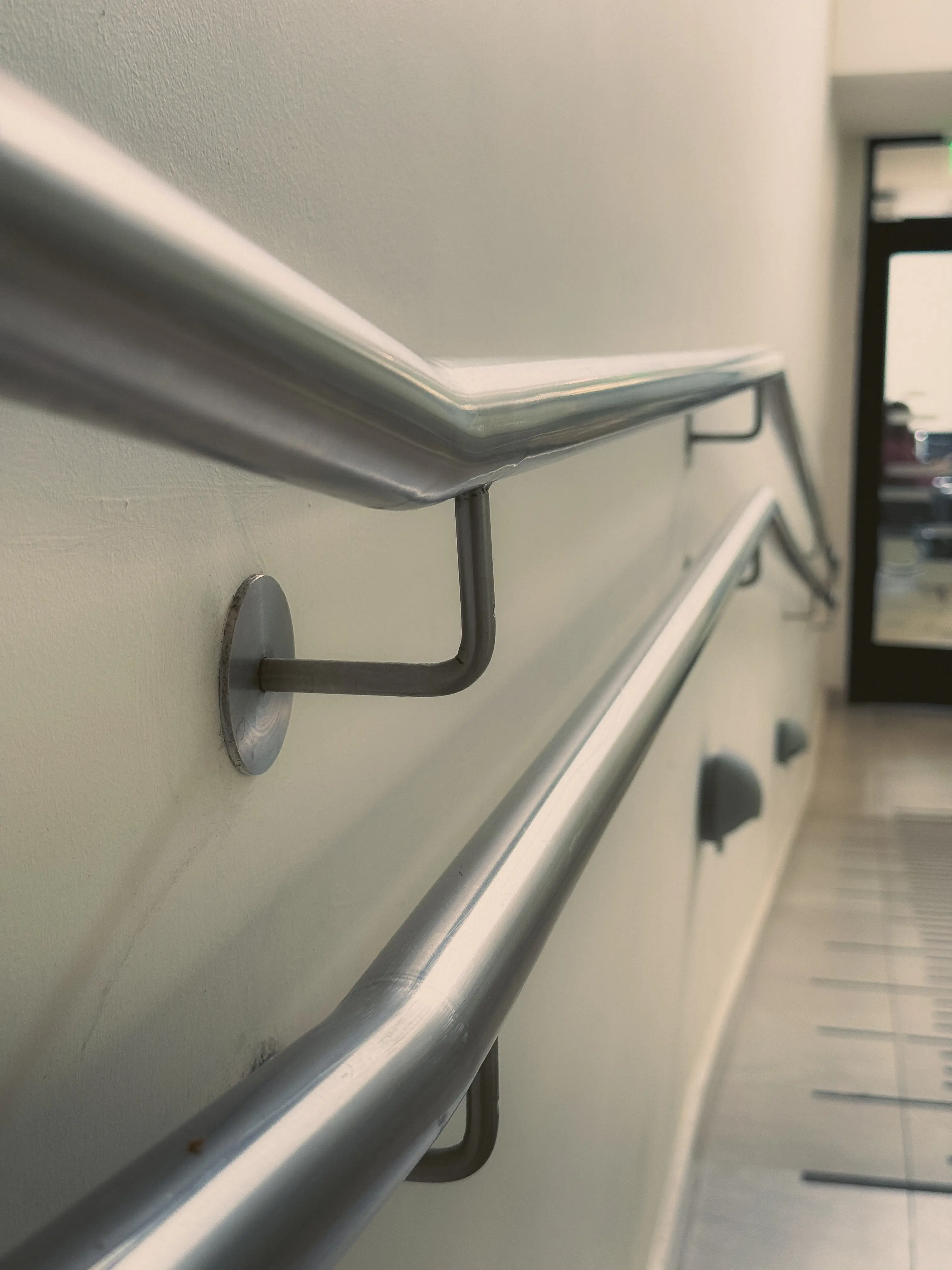 Floating stair railing made of brushed 316L stainless steel. The railing features a minimalist design with clean lines, mounted to the side of a staircase with no visible supports, creating a floating effect. The finish is matte and industrial, complementing the modern architectural style of the space.