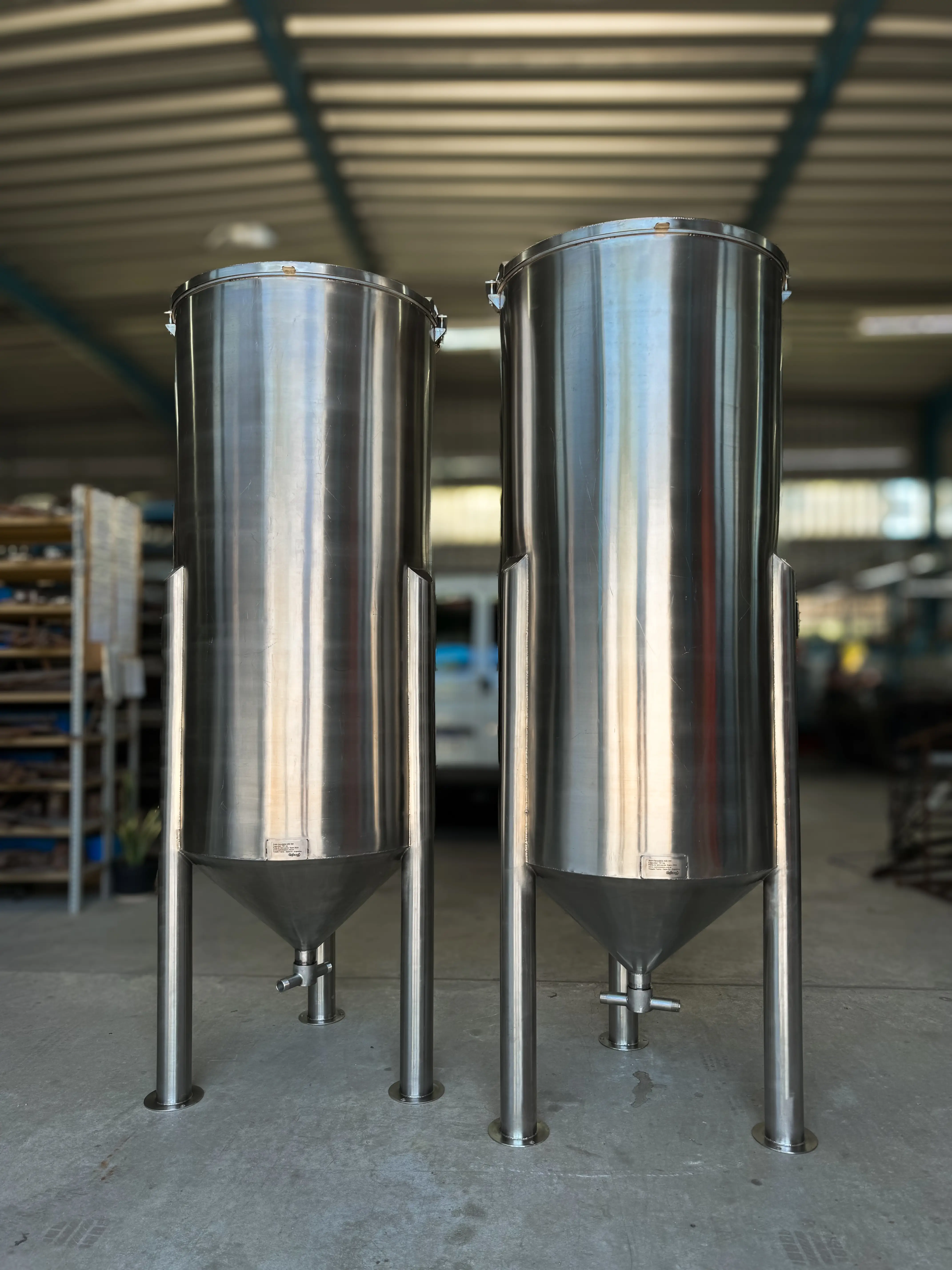 Two 700L mixing tanks made of AISI 304 stainless steel, designed for industrial applications. The tanks feature a cylindrical shape with a conical bottom for efficient mixing and easy discharge of contents. Each tank is equipped with a top-mounted agitator for thorough mixing of liquids, and the polished finish provides corrosion resistance and ease of cleaning, making them suitable for use in food processing, pharmaceuticals, or chemical manufacturing.
